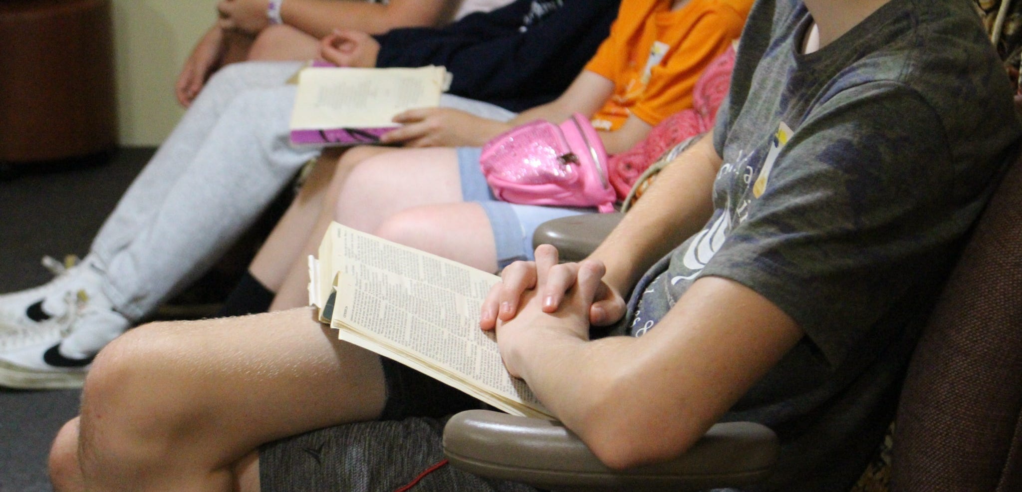 A group of people sitting with their legs crossed, some holding Bibles, indicating a reading or study session.