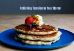 Stacked pancakes topped with syrup, whipped cream, strawberries, and blueberries on a blue plate. Text reads "Relieving Tension In Your Home."